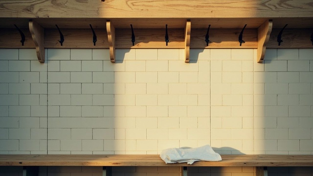 An empty dressing room bench in warm evening light, a folded white towel beneath a row of bare coat hooks