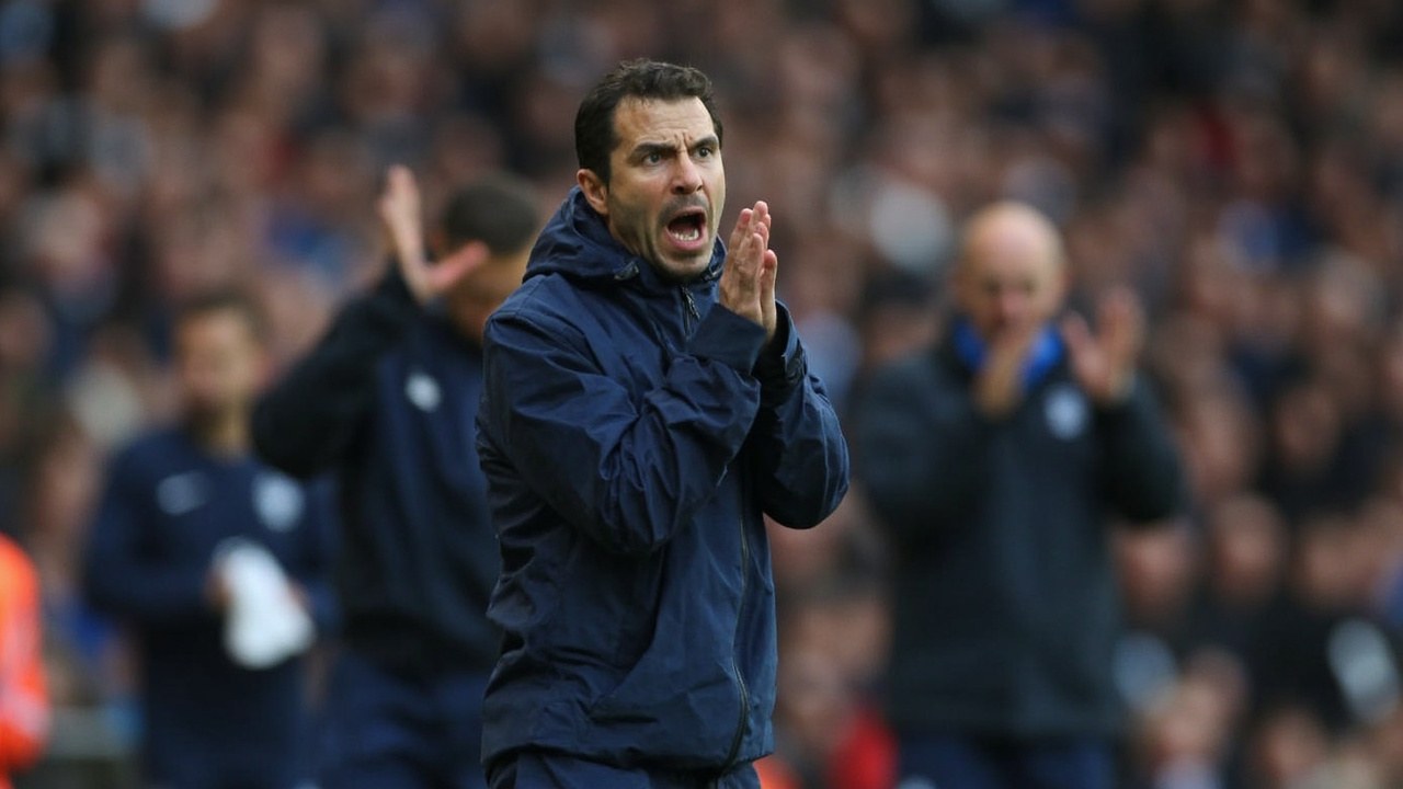 Djed Spence in a navy Spurs away shirt on the touchline at the Vitality Stadium, gesturing for the ball with two raised fingers as Bournemouth defenders retreat toward their own goal in flat afternoon daylight